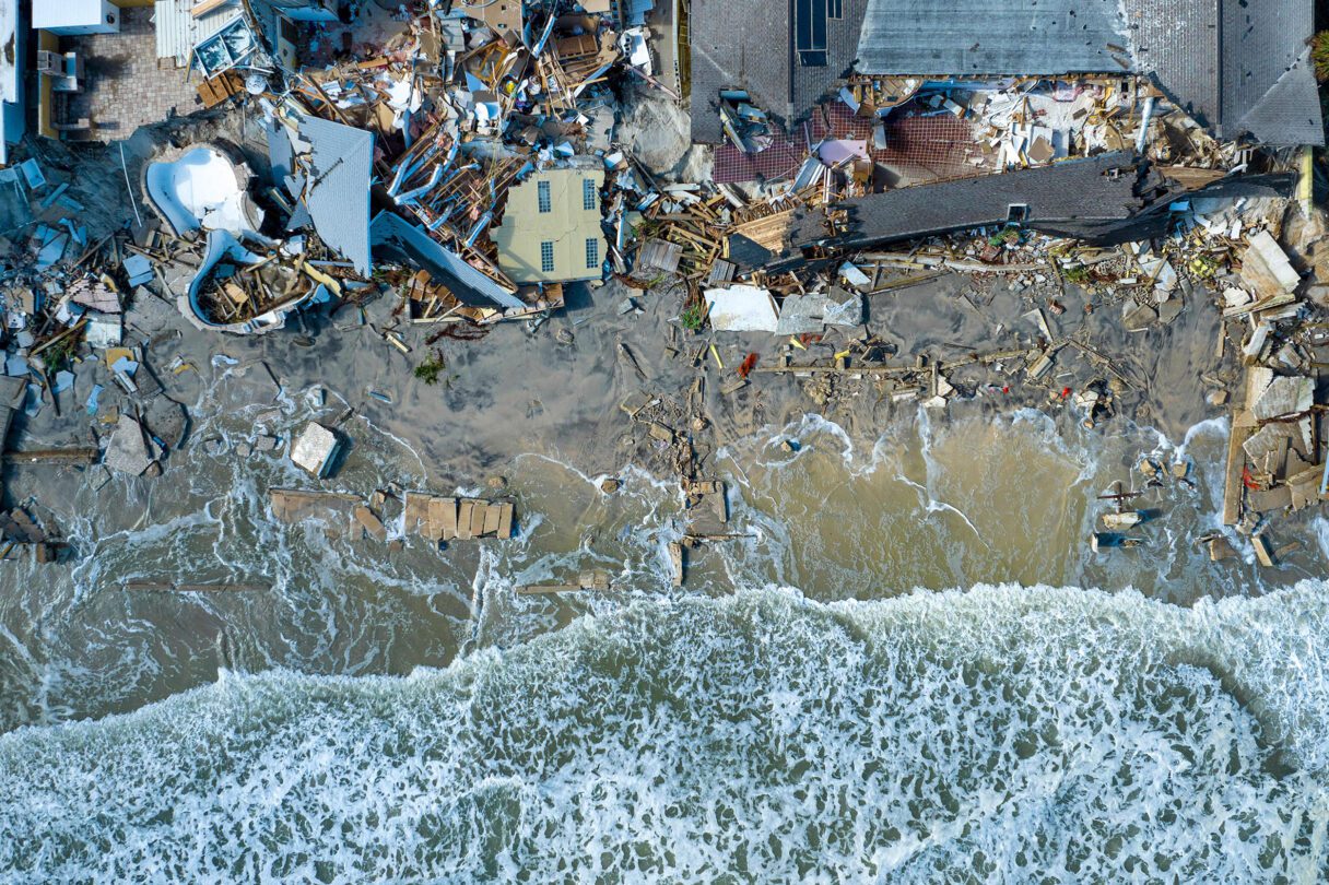 Waves lap piles of wreckage and rubble from destroyed houses on a beach.