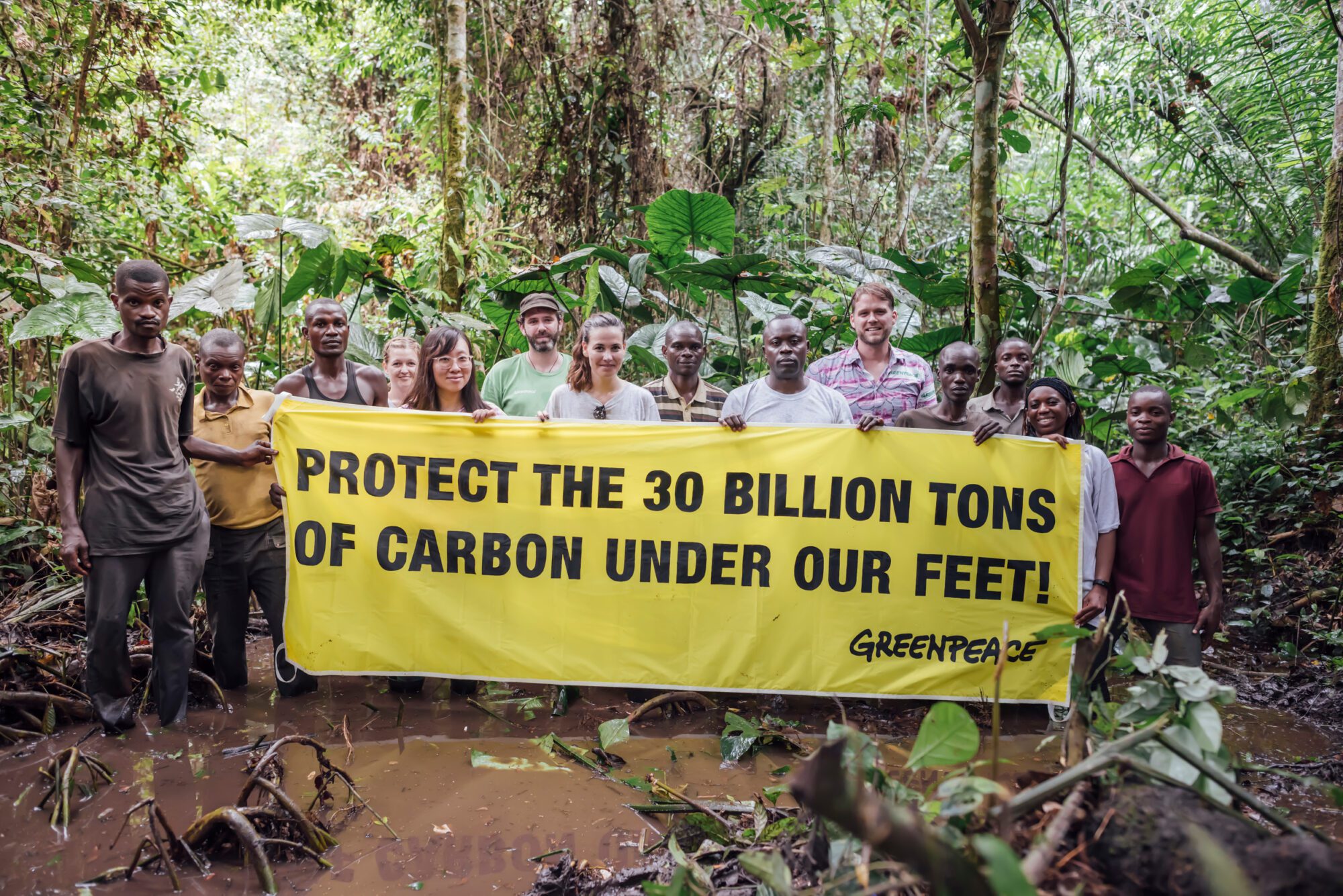 Group of people in a wetland forest hold a banner saying "Protect the 30 billion tons of carbon under our feet!"