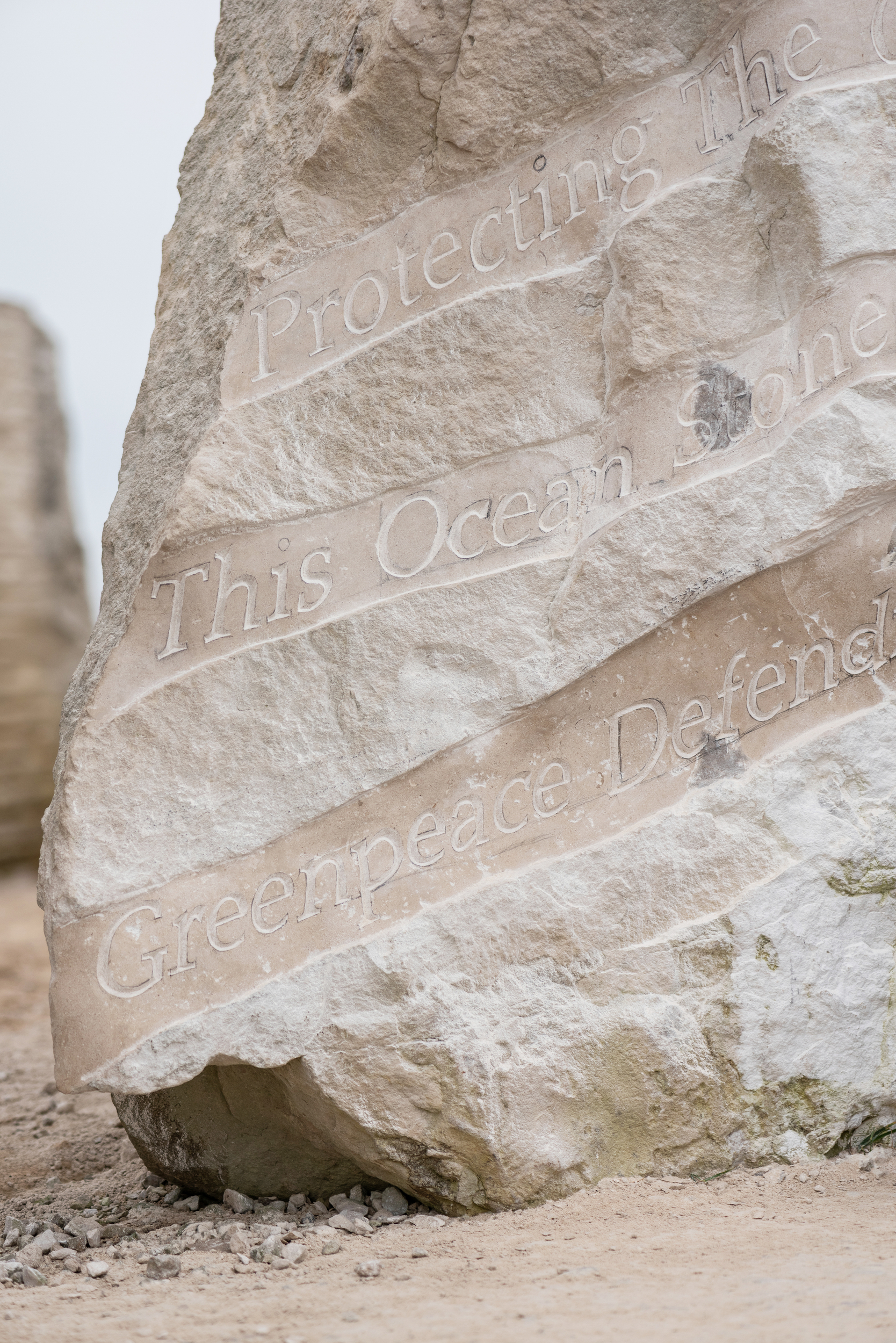 Close-up of carved text on a large stone. The fragments of text visible say: "Protecting the", "This ocean stone" and "Greenpeace defend"