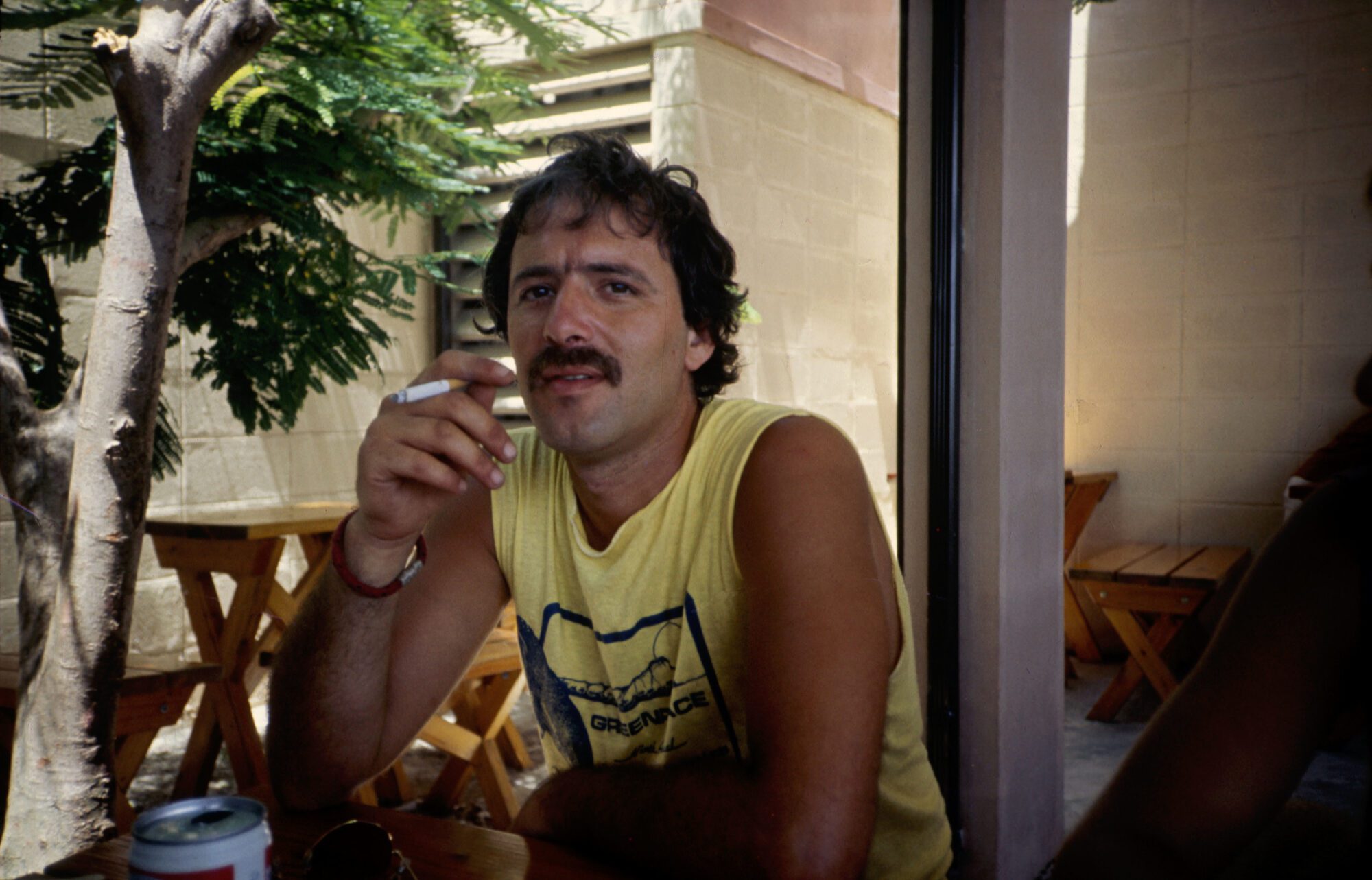 Fernando Pereira wearing a yellow vest, smoking a cigarette. He's looking into the camera with a relaxed expression.