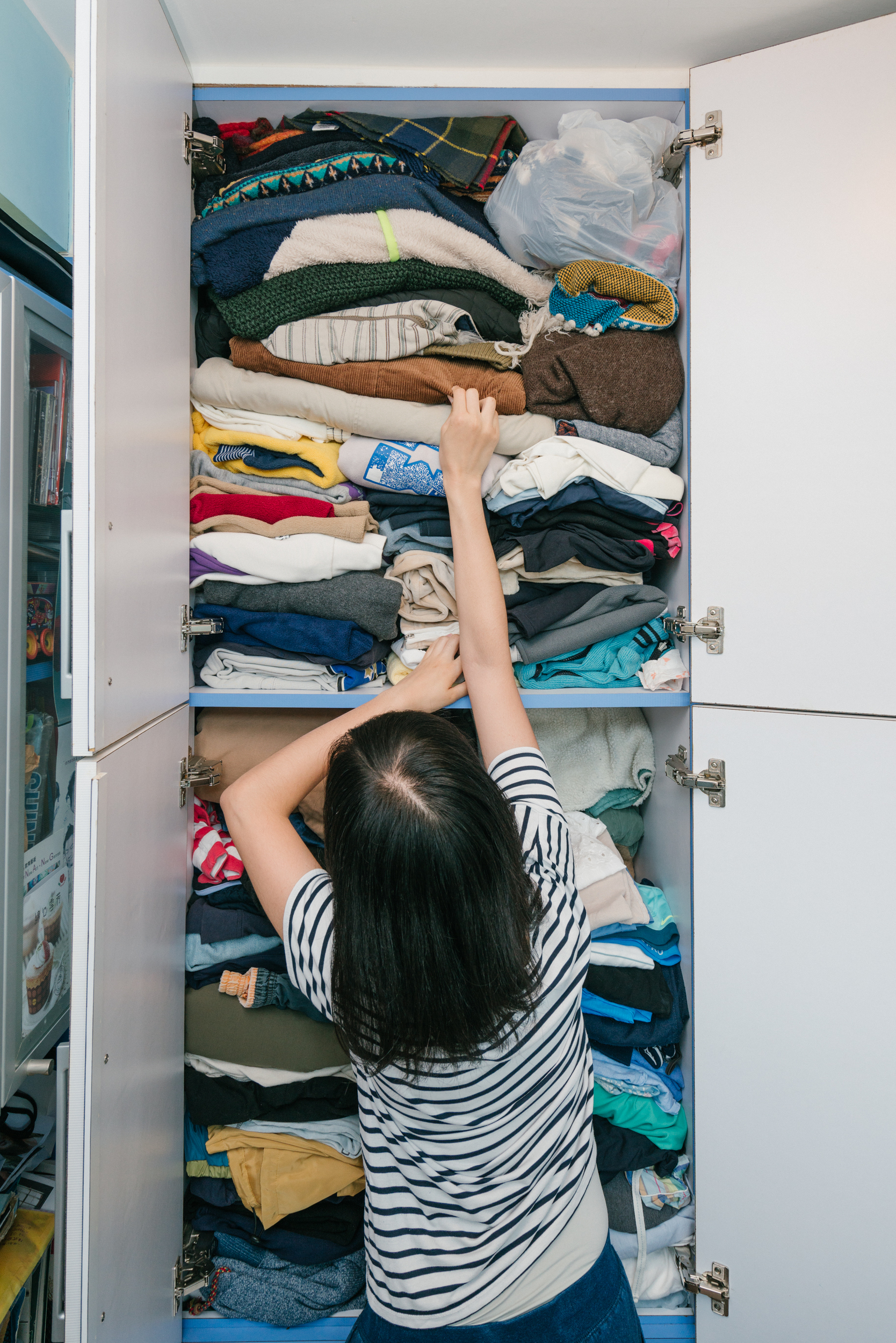A woman reaches high into her open wardrobe crammed with clothes