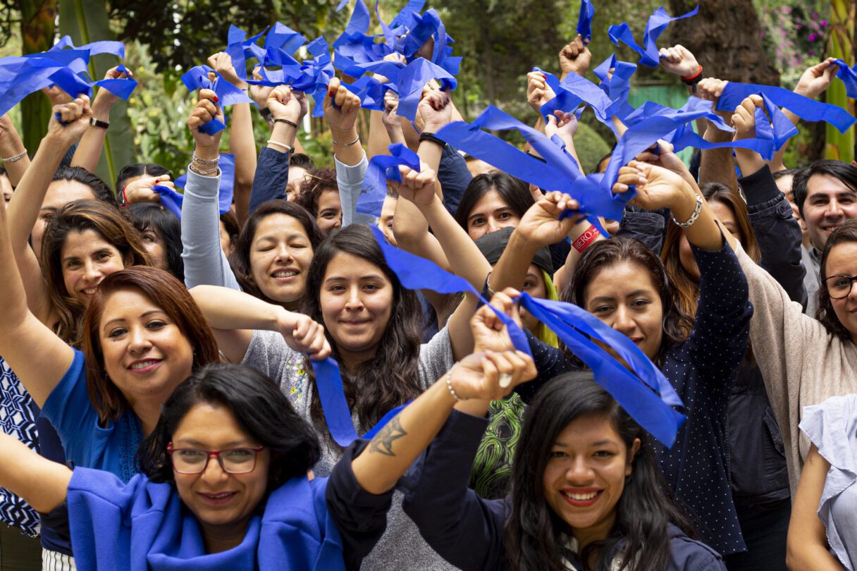A crowd of people hold up pieces of blue fabric as they smile into the camera.