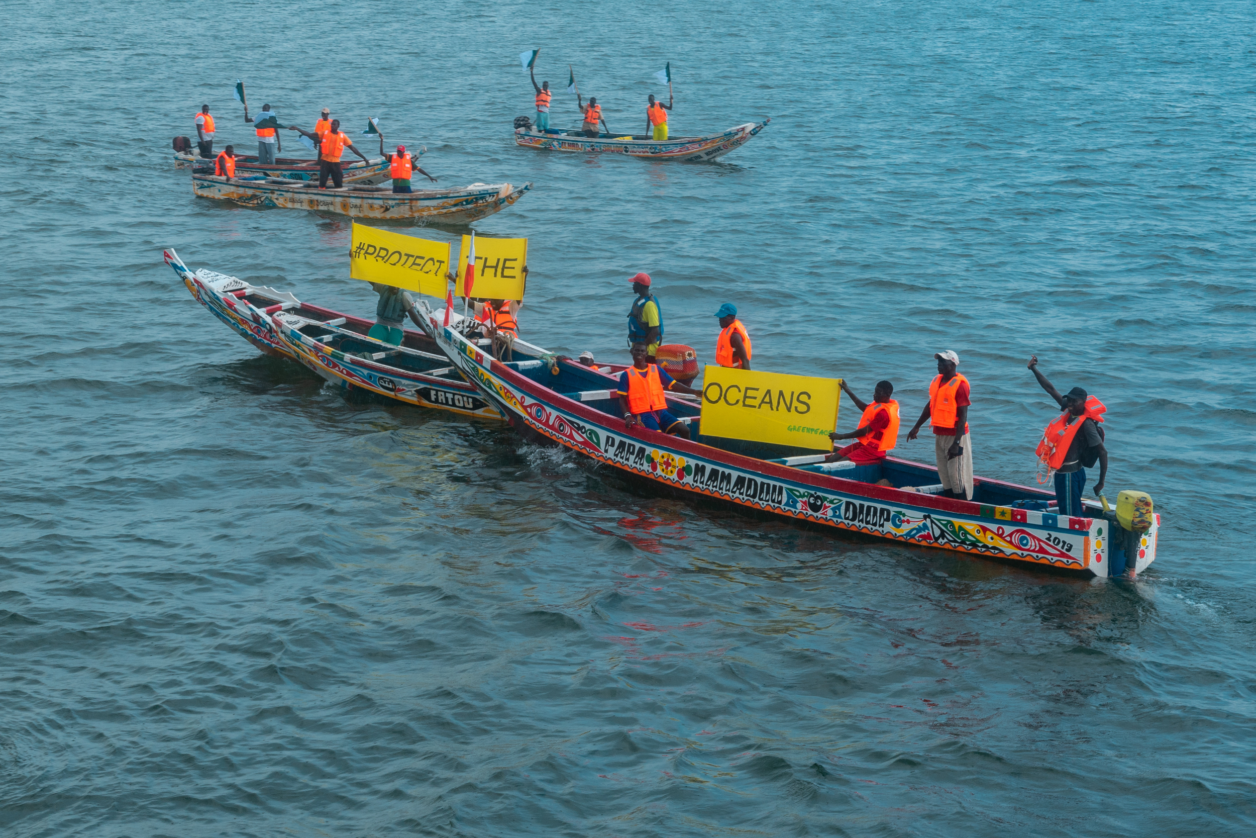 Local fishermen on colourful traditional boats display banners with various messages including “Protect the Oceans” and “Stop Fishmeal”.