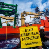 Activist on a boat alongside a ship holds up a stop deep sea mining banner