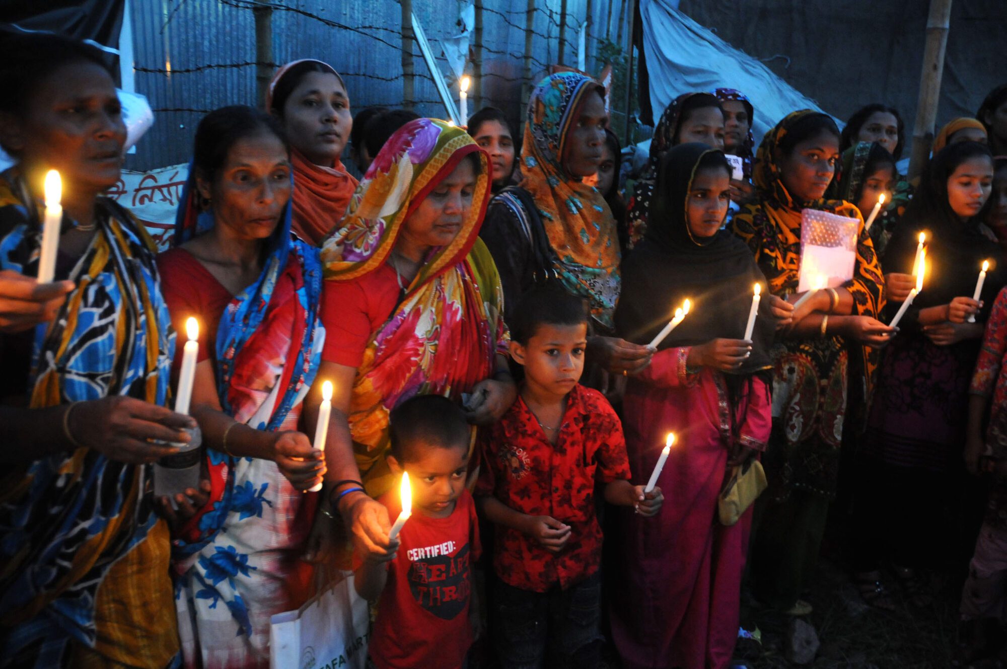A group of women and children sombrely hold candles.