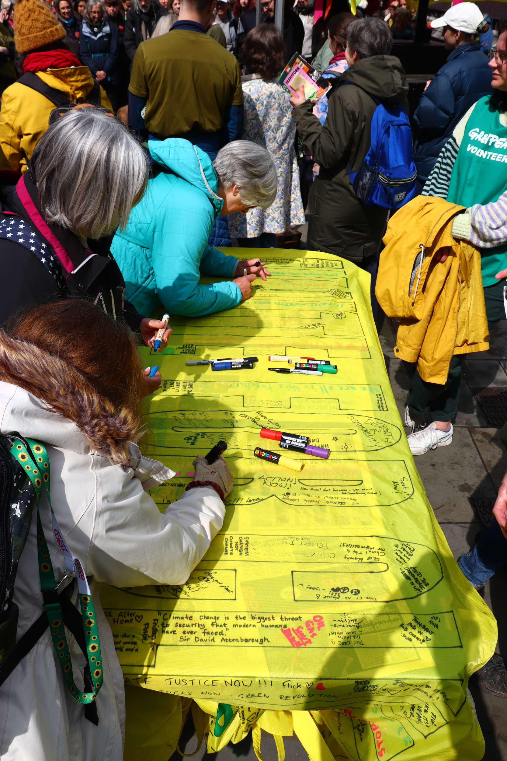 People writing on a large yellow banner laid out on a trestle table.