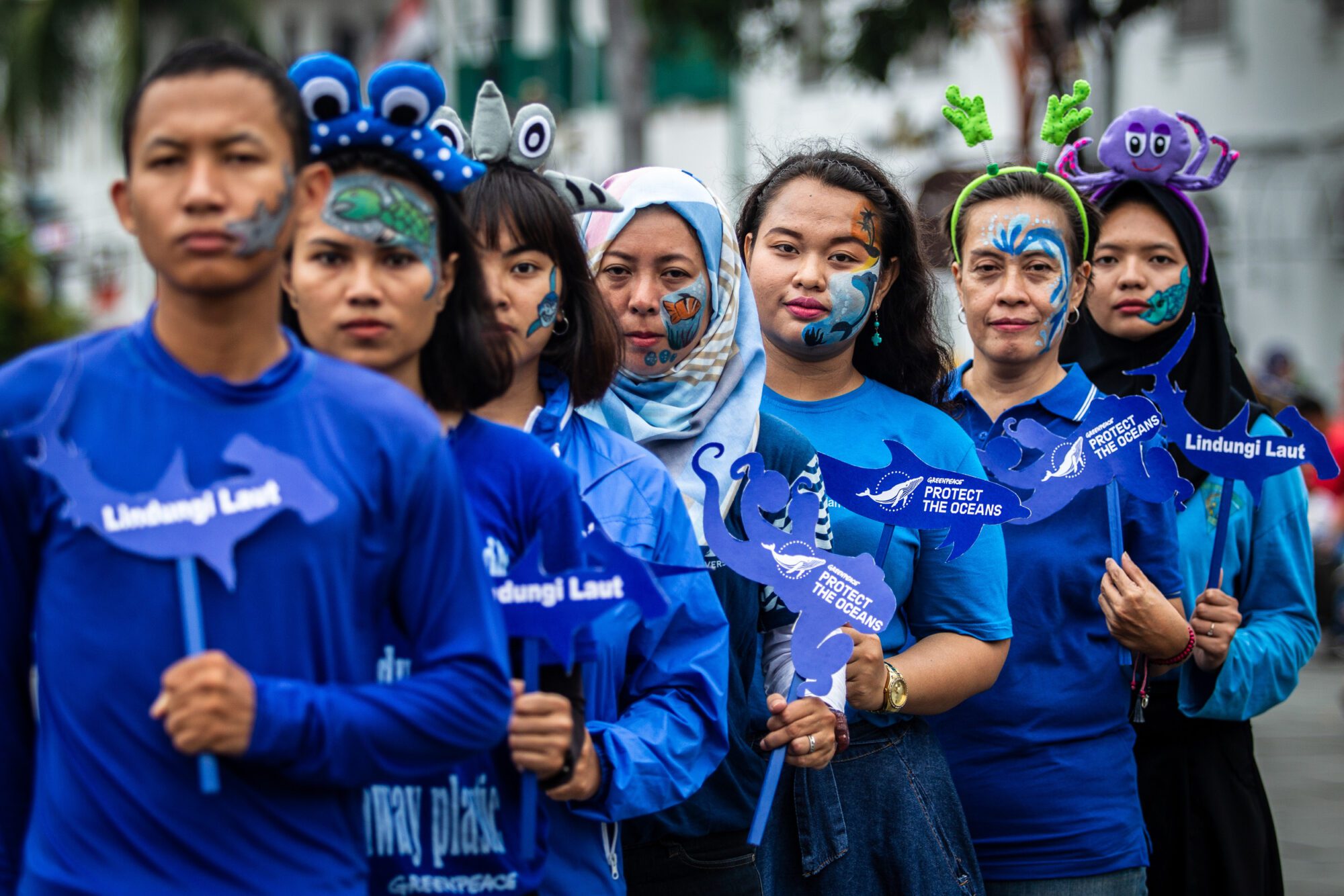 A row of people in blue clothes and ocean themed face paint at a campaign event.