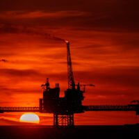 Three connected gas platforms (they look like oil rigs) against a deep red sunset.