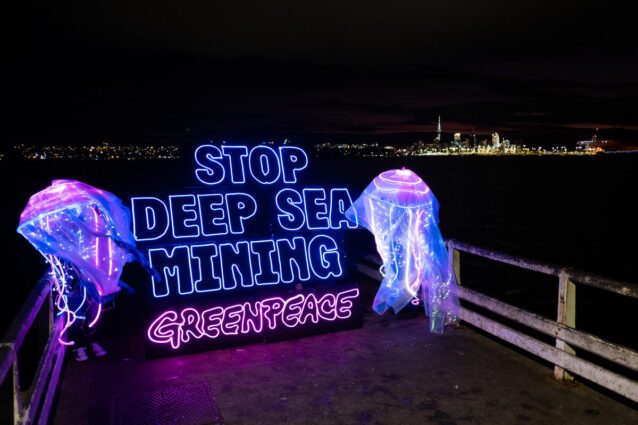 Neon sign saying stop deep sea mining with jellyfish sculptures on each side
