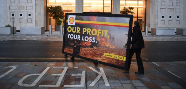 Activists carry a billboard with a spoof Shell advert showing a wildfire with the slogan our profit your loss