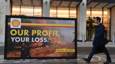 Activists carry a billboard with a spoof Shell advert showing a wildfire with the slogan our profit your loss