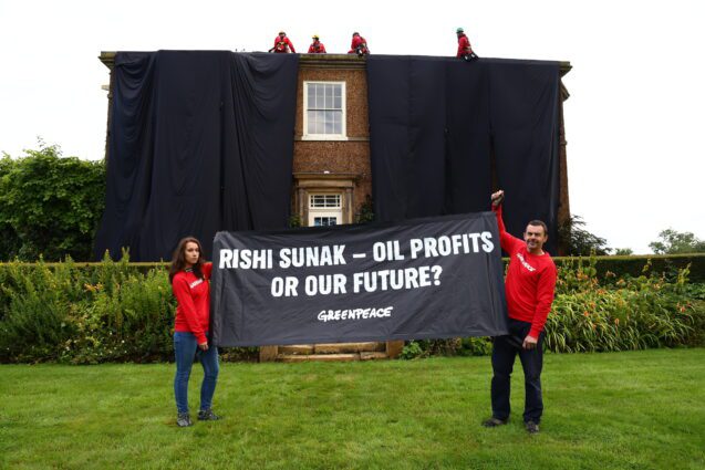 Activists hold a banner reading 'Rishi Sunak - oil profits or our future?' In the background there's a grand house covered in black fabric.