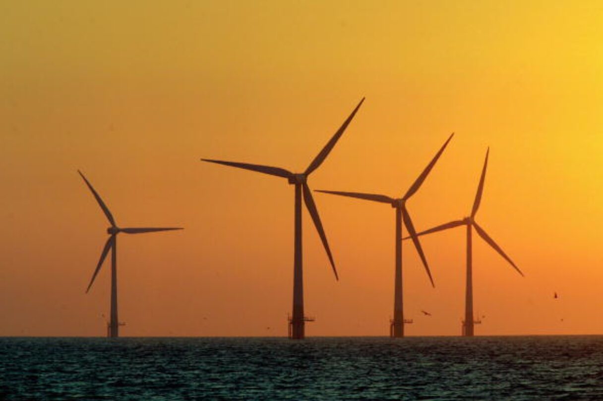 Offshore wind turbines silhouetted against a golden sunset