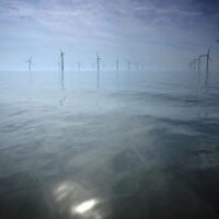 Offshore wind turbines in a reflective calm ocean with light mist
