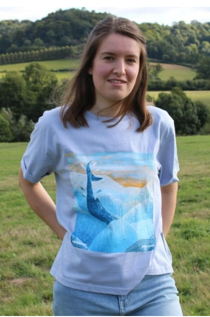 Model wears a tshirt with a whale and iceberg design in subtle pastel colours