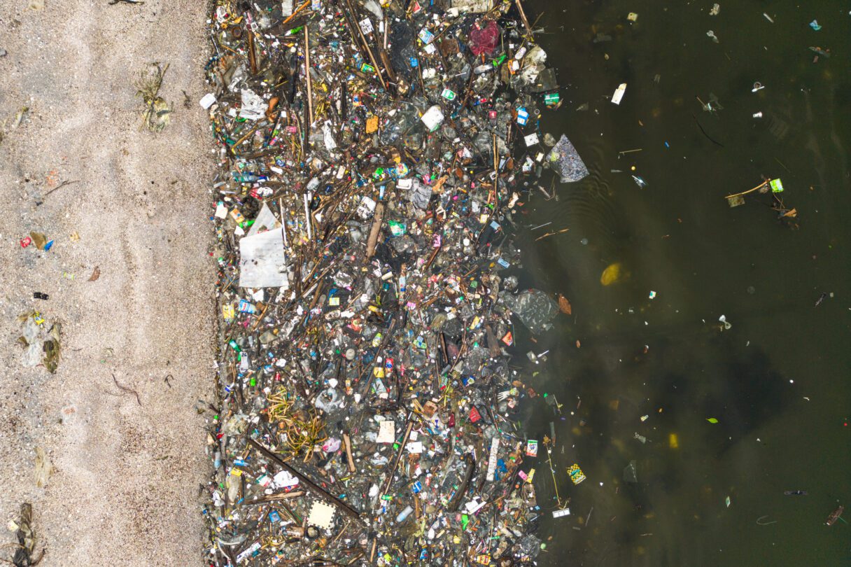 Aerial view of a thick soup of plastic waste clustered along the waterline of a beach.