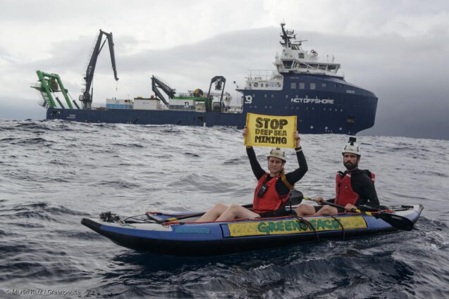 Greenpeace activists in an inflatable boat hold a hand banner reading Stop Deep Sea Mining in front of a mining research vessel in the Pacific