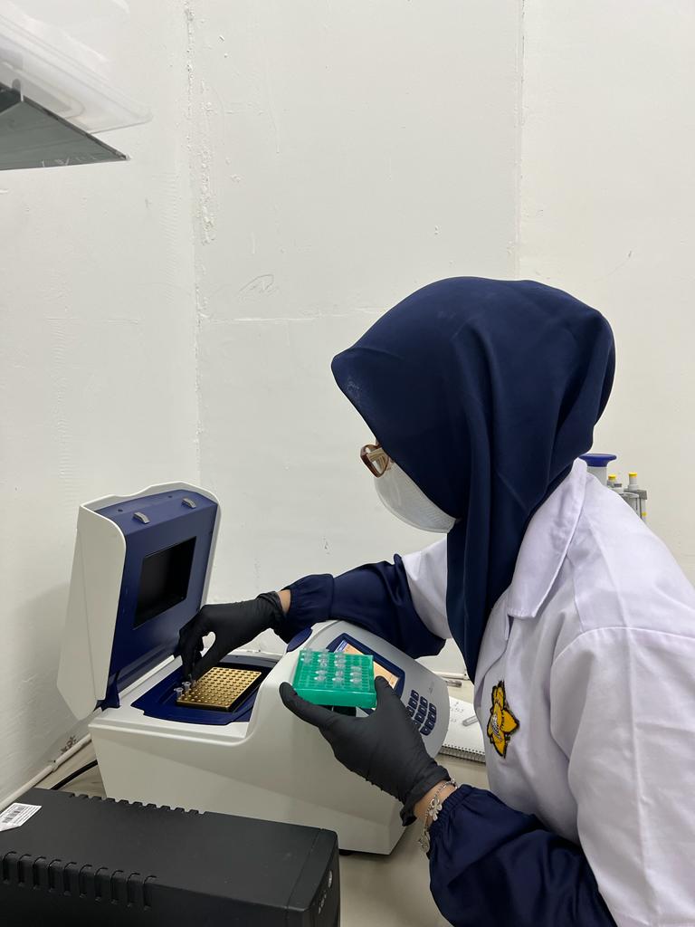 A researcher in a mask and headscarf adds samples to a machine in a laboratory