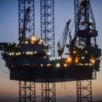 A drilling structure platform lit up at dusk, silhouetted against the blue-orange sky