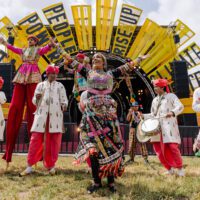 Performers dressed in bright costumes in the Greenpeace field at Glastonbury.