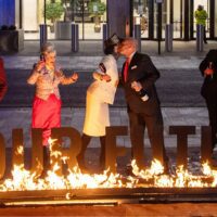 Activists dressed in suits perform as Shell shareholders. In the foreground, burning letters spell out 'our future'.