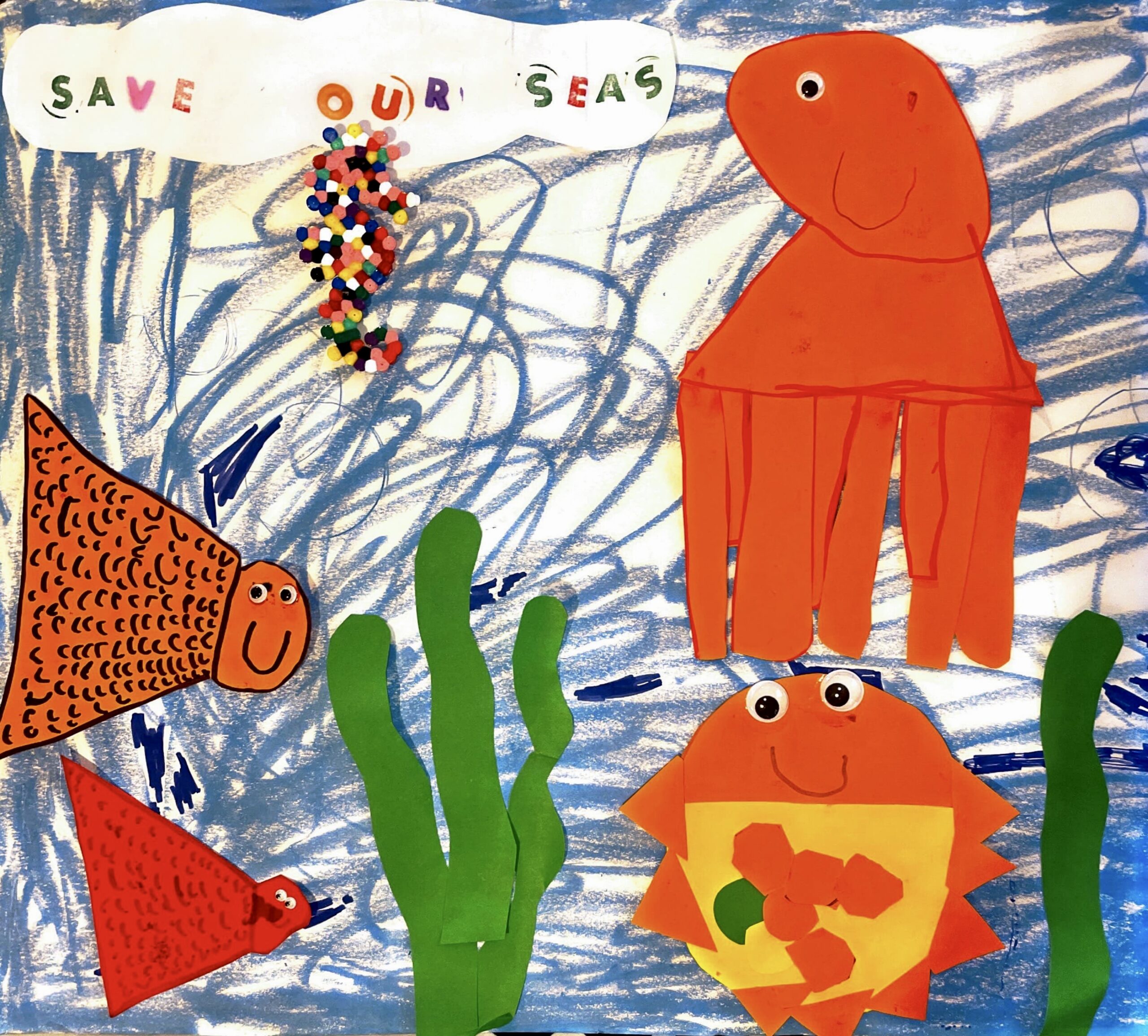 Child’s drawing showcasing oceans wildlife drawn in different coloured paper with googly eyes stuck on, seaweed drawn with green paper and a seahorse drawn out of different coloured beads. As well as a slogan reading ‘save our oceans’