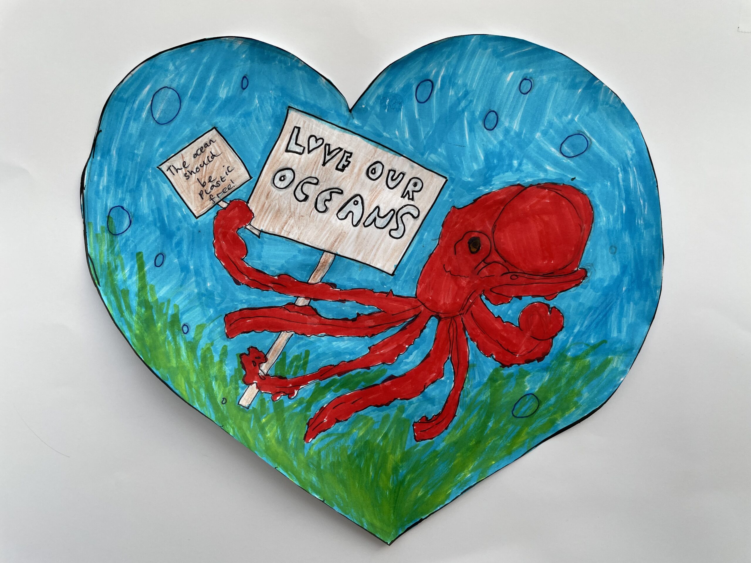 Child's felt pen drawing shows a red octopus holding up a placard that reads 'Love our oceans'.
