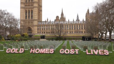 The lawn in front of the UK parliament building is covered in hundreds of mock gravestones in rows. Funeral style wording in flowers reads 'cold homes cost lives'.