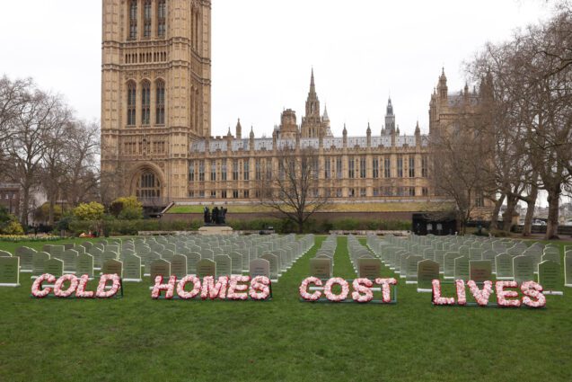 The lawn in front of the UK parliament building is covered in hundreds of mock gravestones in rows. Funeral style wording in flowers reads 'cold homes cost lives'.