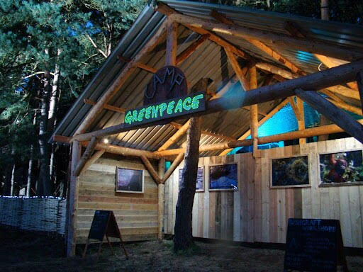 An inviting-looking wooden building lit up at night. Sign on the front says 'camp greenpeace.