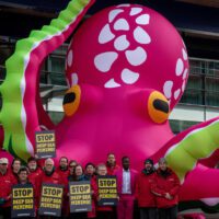 An inflatable pink octopus stands outside a tall hotel in London's canary wharf. A Greenpeace activist holds a banner reading 'STOP DEEP SEA MINING' in front.
