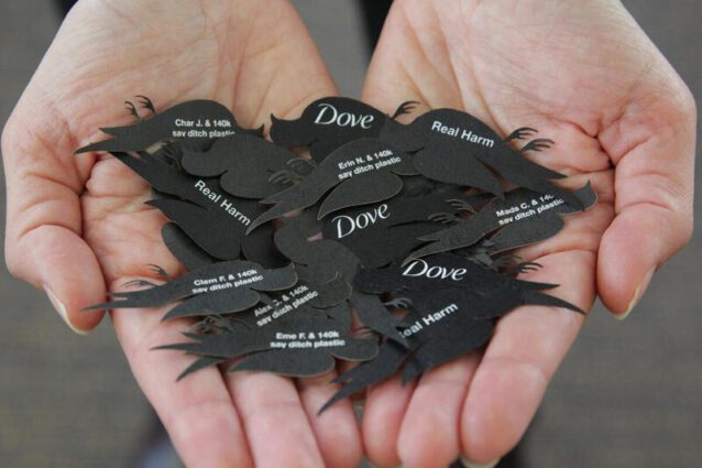 Hands open a pile of small black paper birds . reading names one one side and the Dove logo on the other