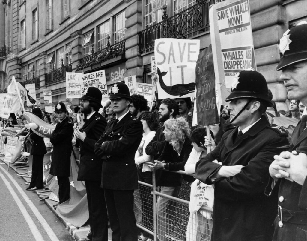 Large group of protestors with banners outside a building, with police standing guard in front