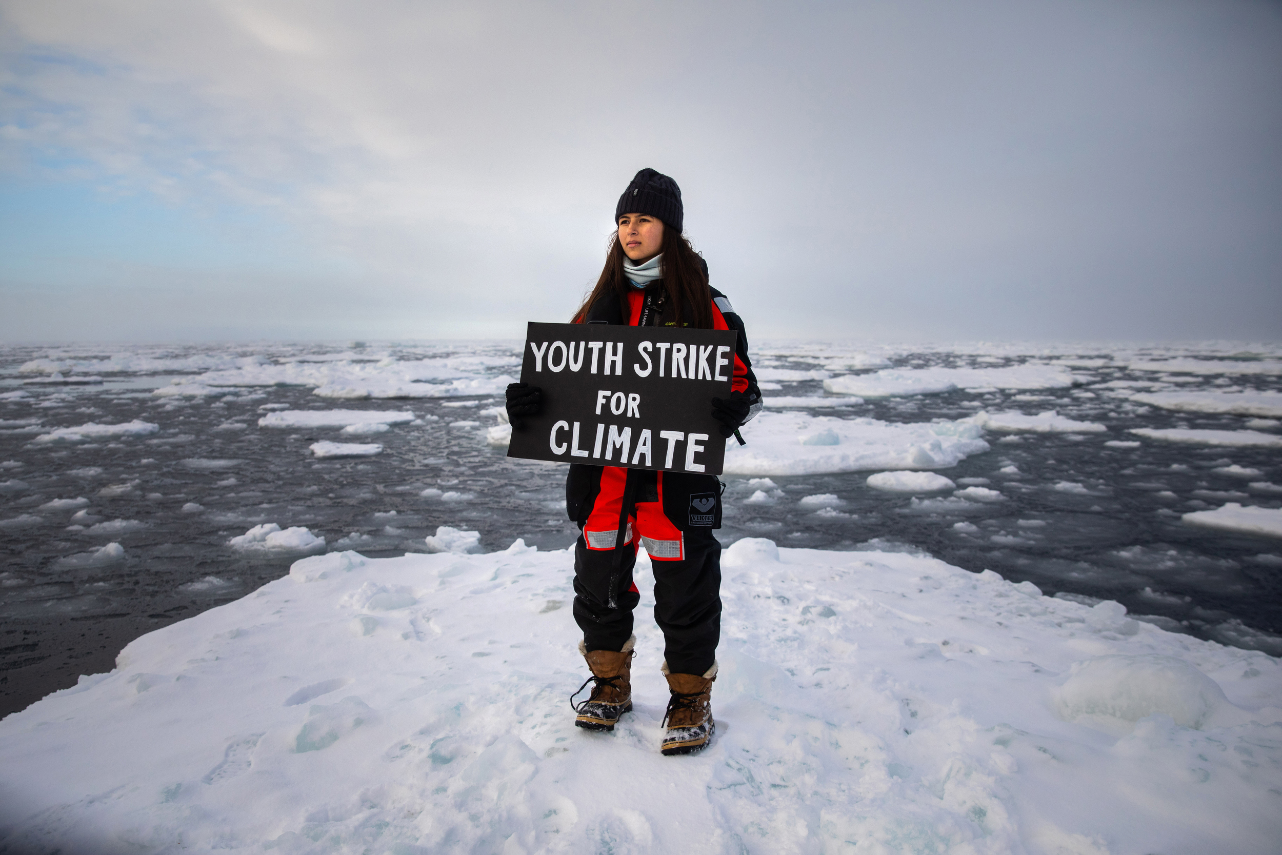 Youth activist Mya-Rose Craig stands on an ice floe holding a hand-painted sign reading "Youth strike for climate"