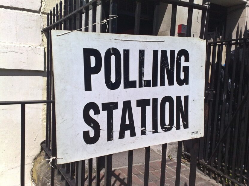 A black on white sign reading Polling station, pinned onto a fence