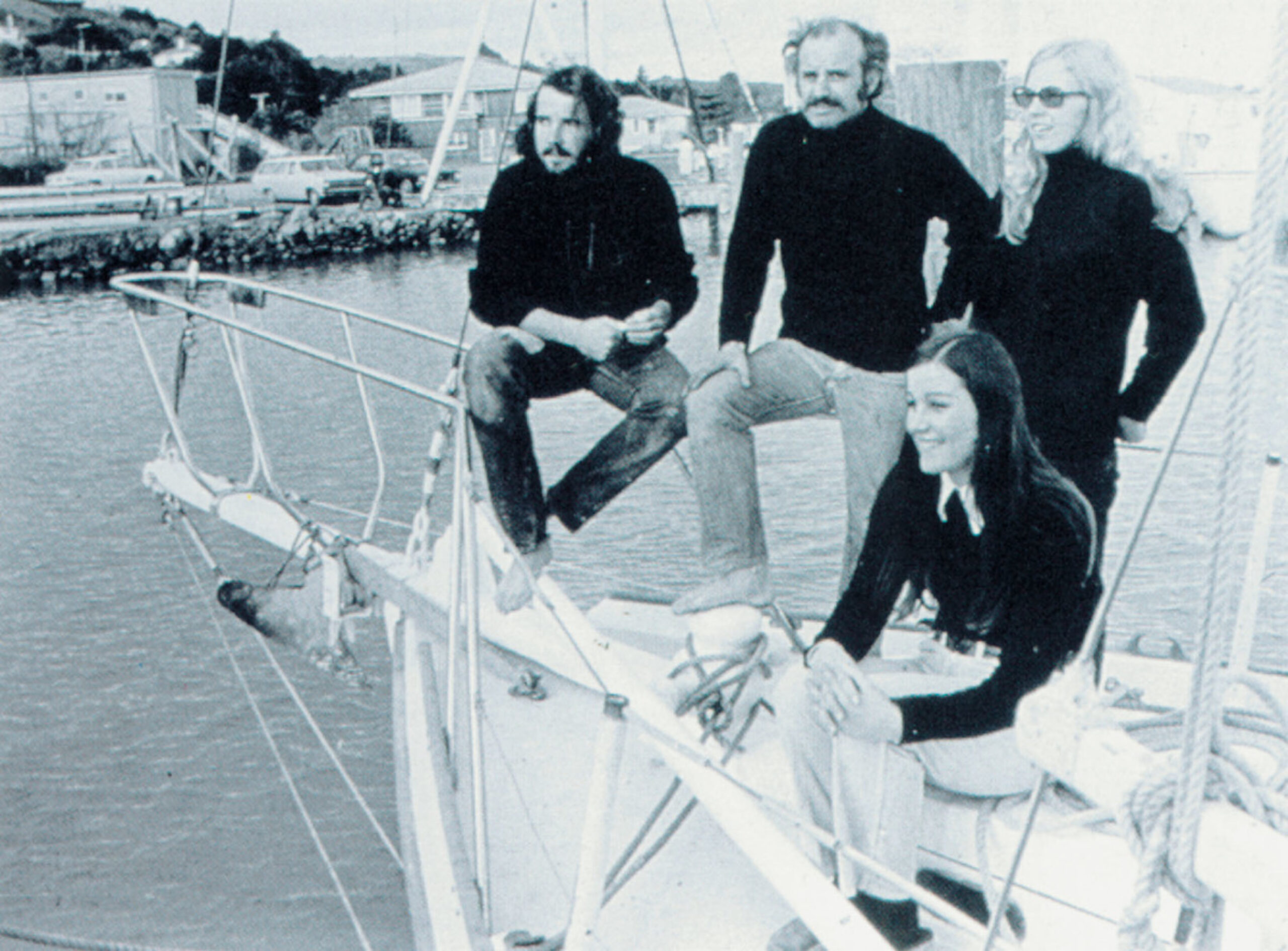 Black and white photo of two men and two women sitting on the prow of a boat in black tops.