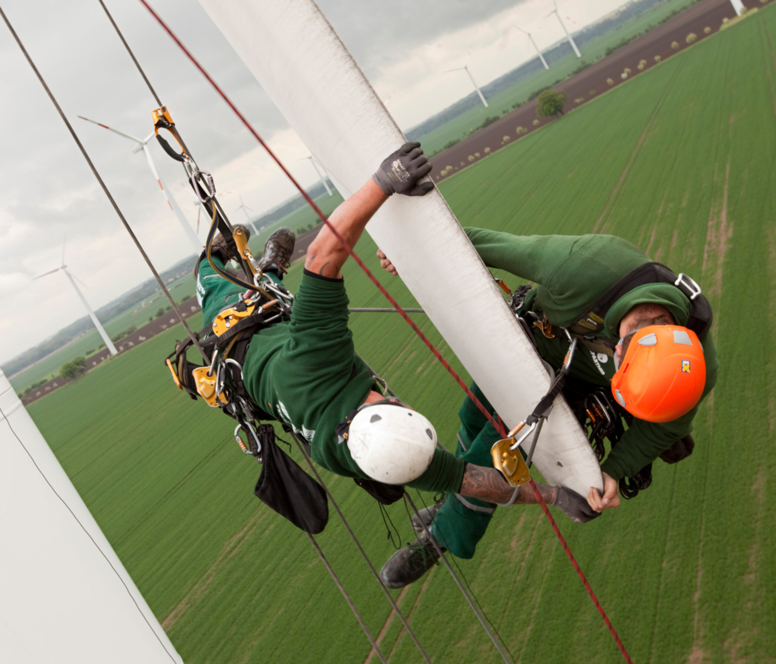 Workers hanging from ropes inspect a wind turbine blade high in the air. A just transition should help workers find jobs in emerging green industries.