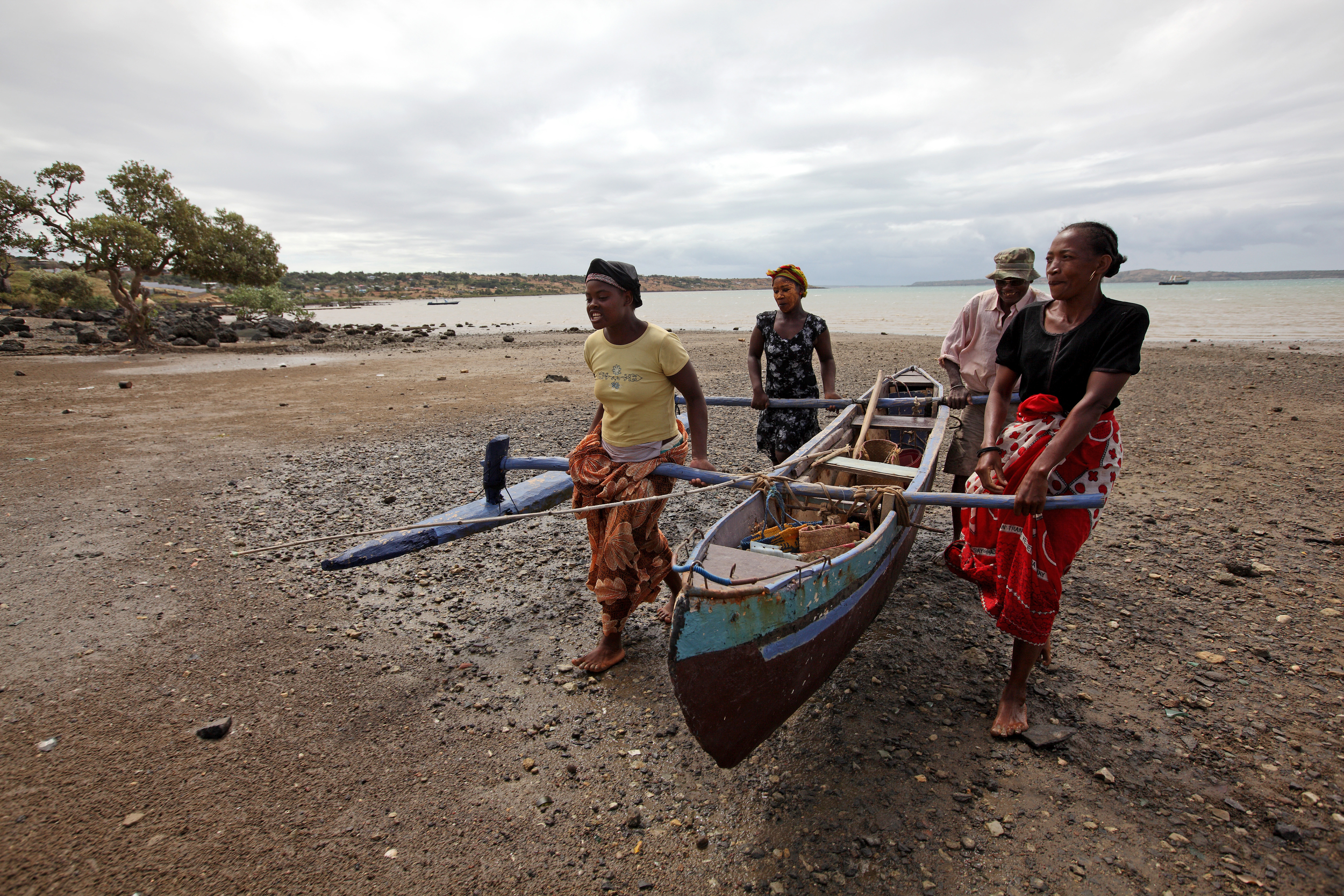 A group of people carrying a traditional wooden fishing boat up a beach