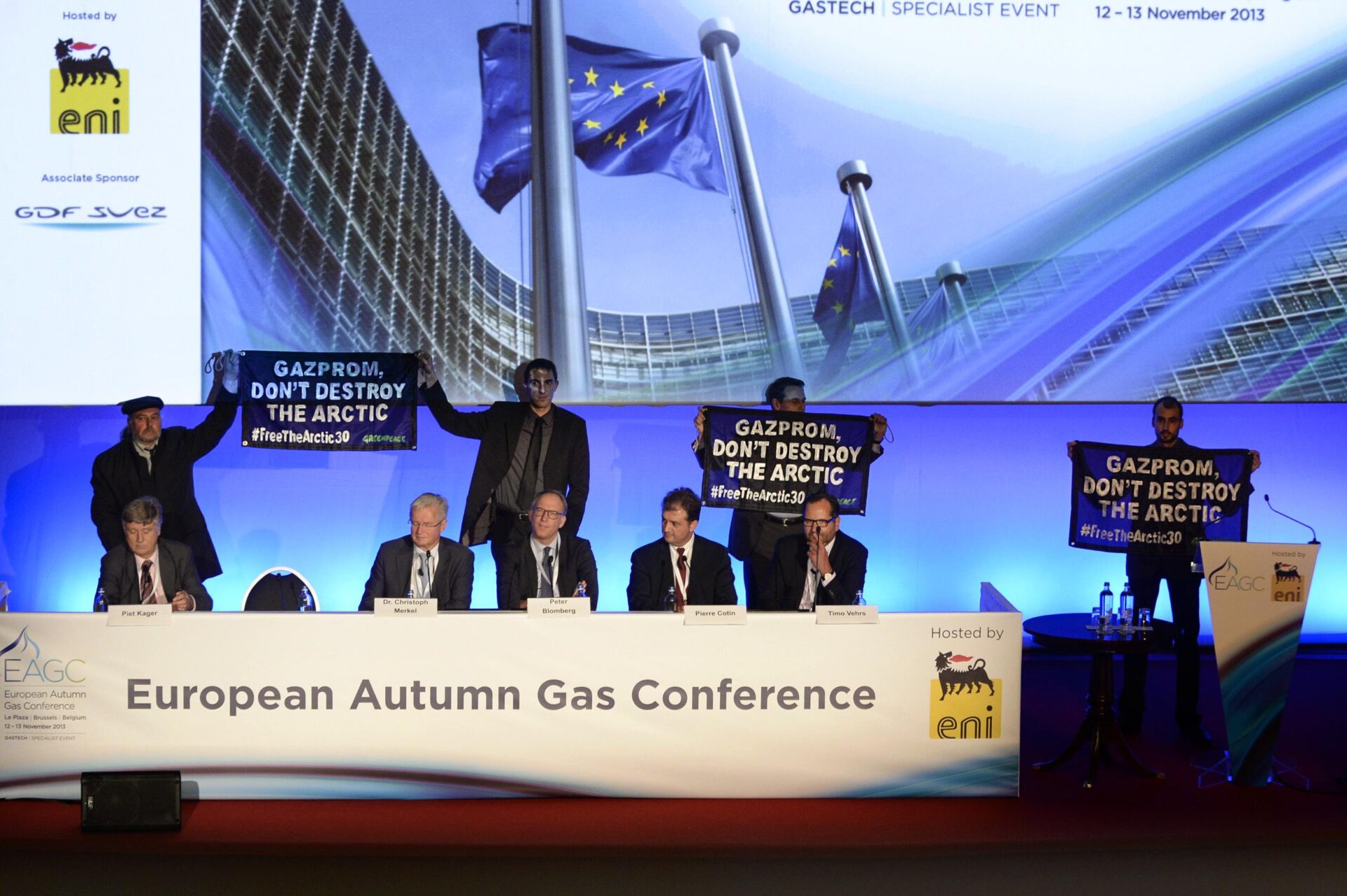 Activists stand behind a row of three seated corporate executives. Their banner reads 'Gazprom, don't destroy the Arctic'