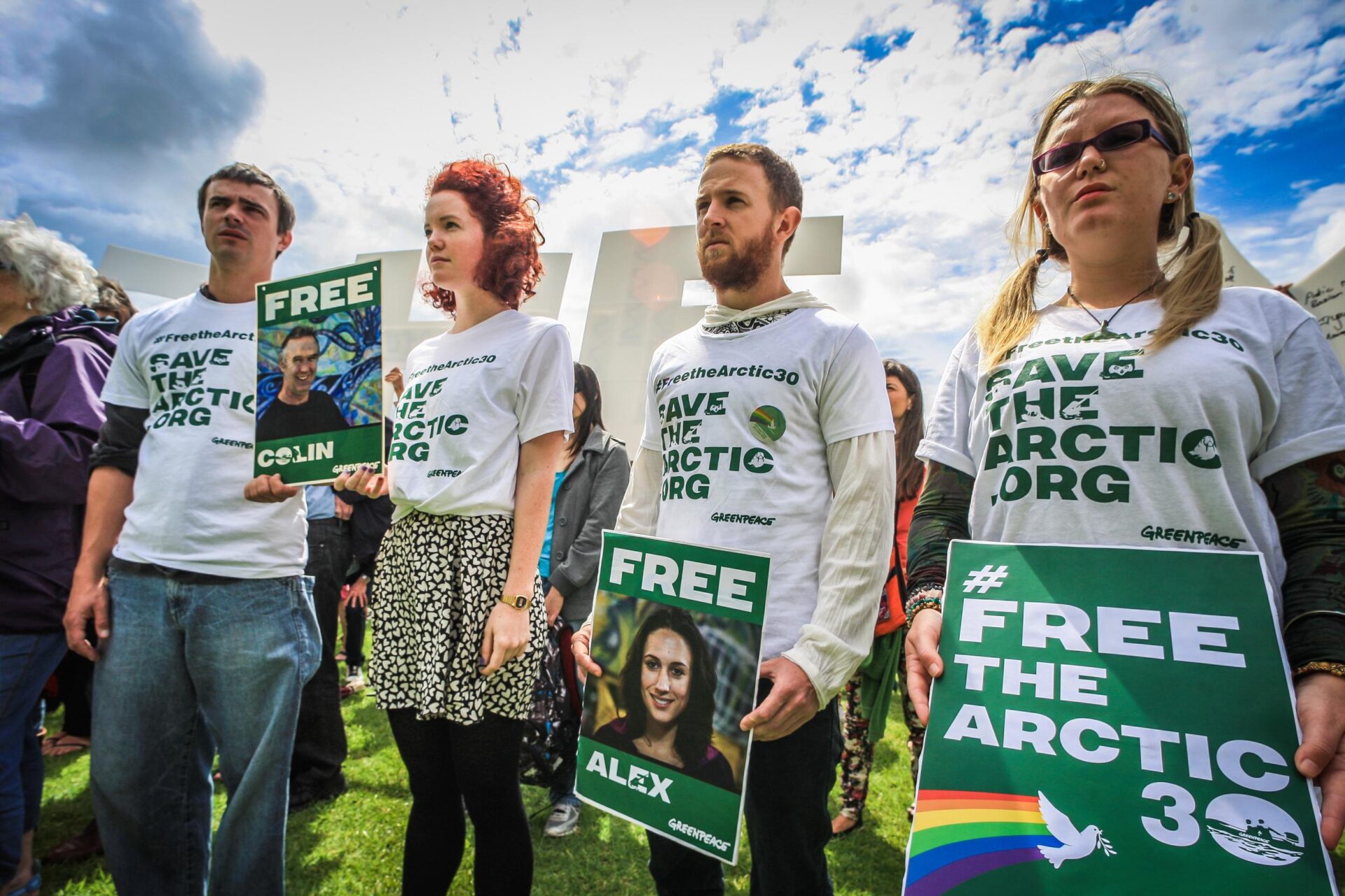Activists wearing campaign t-shirts hold up signs saying 'Free Alex', 'Free Colin' etc.