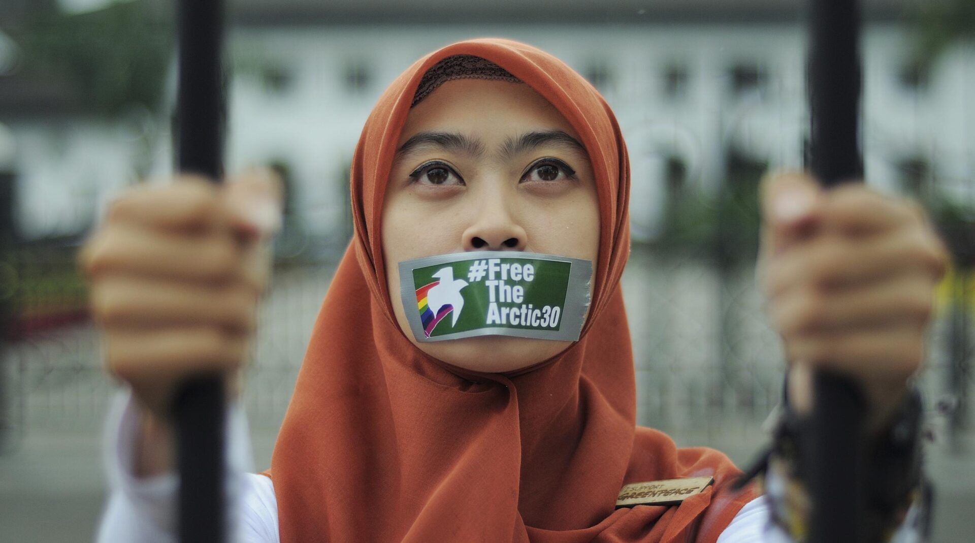 Closeup of an activist's face with tape over her mouth and a sticker saying 'Free the Arctic 30'