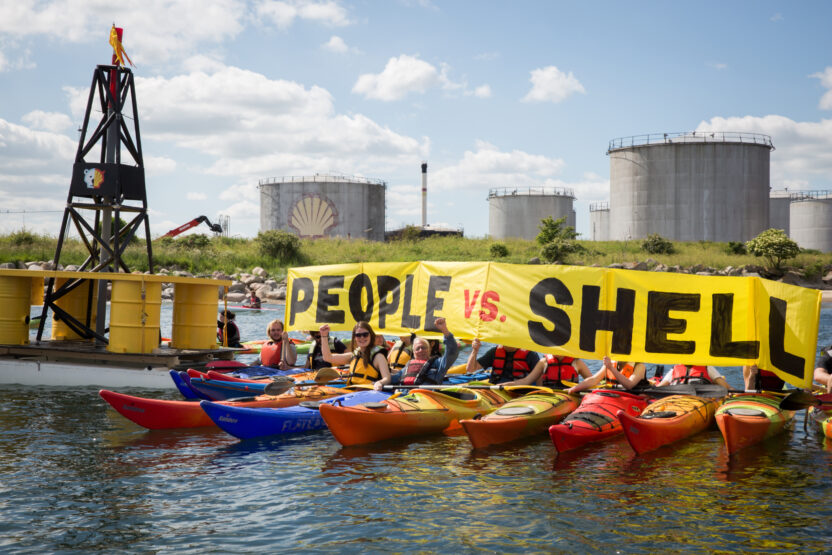 A row of people in colourful kayaks hold up a banner reading 'People vs Shell'