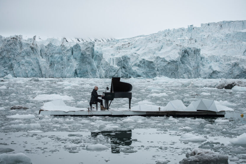 A man playing a grand piano on an island in the Arctic, surrounded by iceberg and ice floes