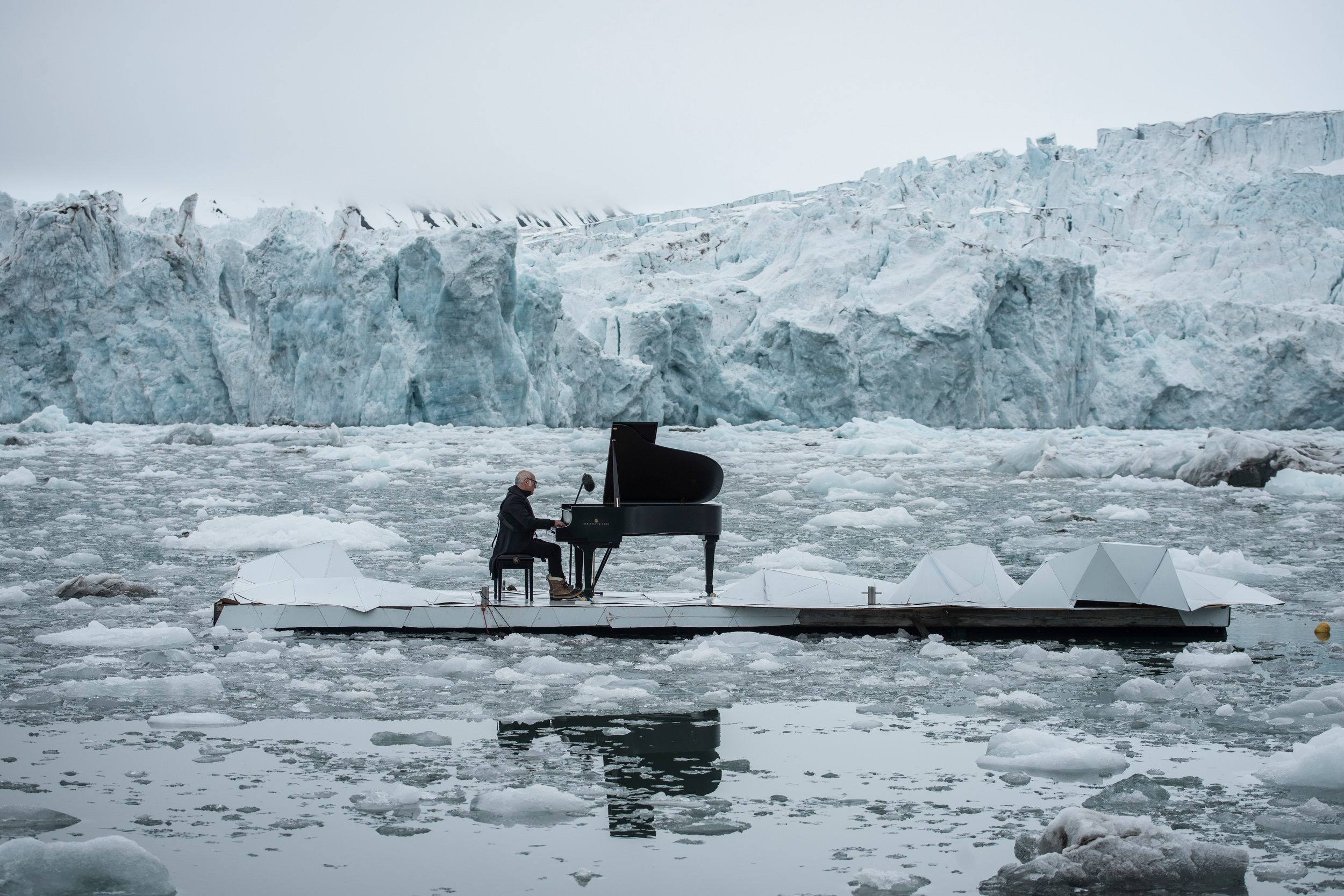 A man playing a grand piano on an island in the Arctic, surrounded by iceberg and ice floes