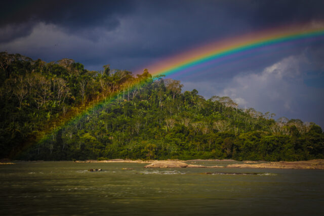Rainbow over a river. Trees gently slope up from the river bank.