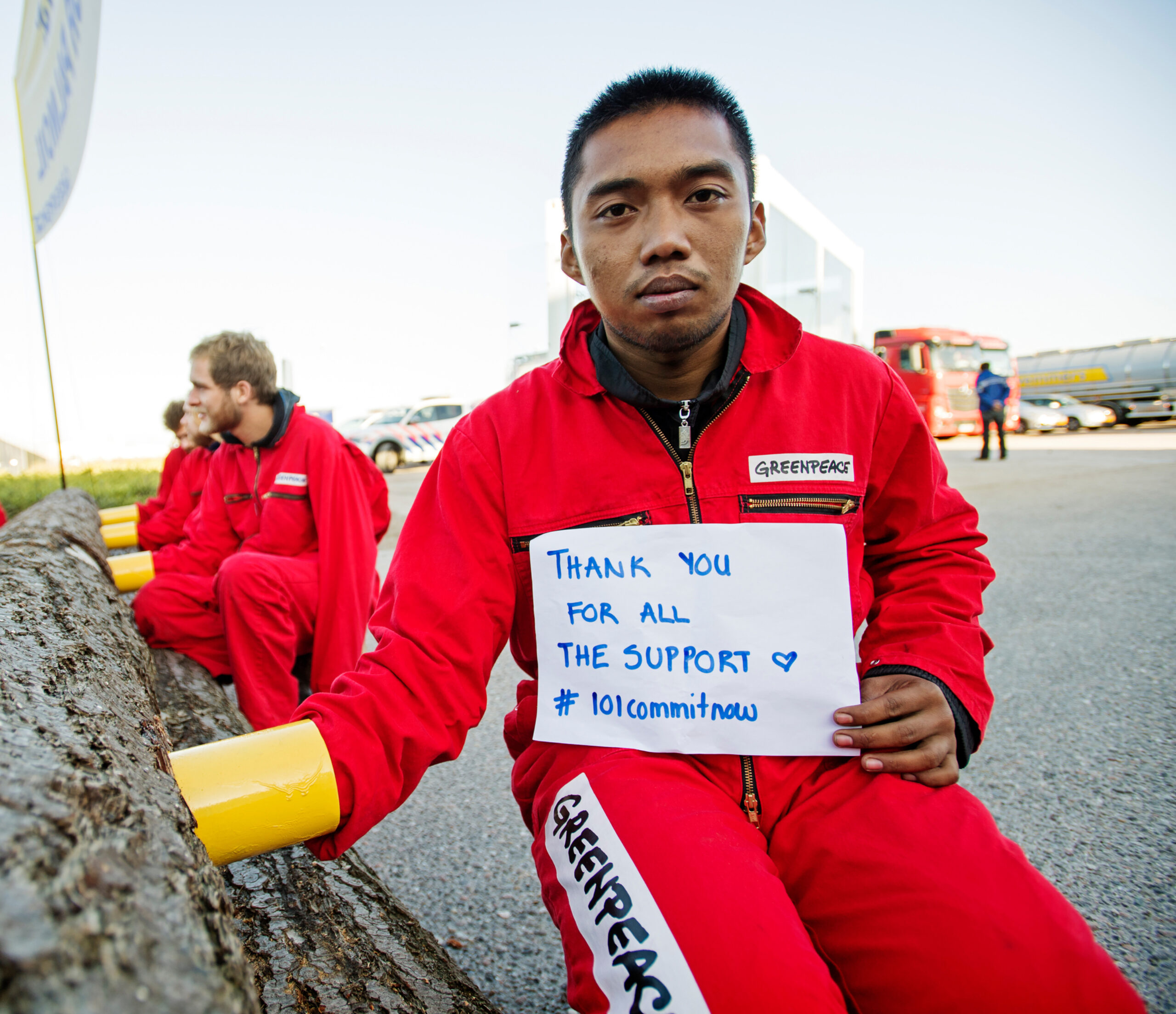 A protestor locked to a giant log holds a sign saying thanks for the support.