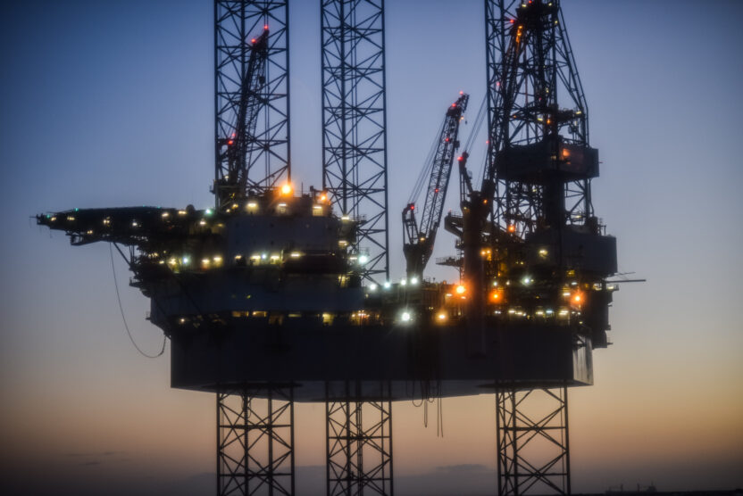 A drilling structure platform lit up at dusk, silhouetted against the blue-orange sky
