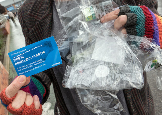Close up of someone's hands holding plastic packaging and a Greenpeace flyer with a note to supermarket store managers