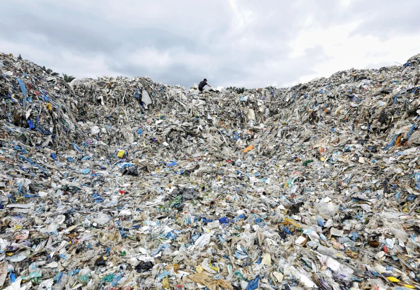 A worker stands at the top of a giant mound of plastic waste