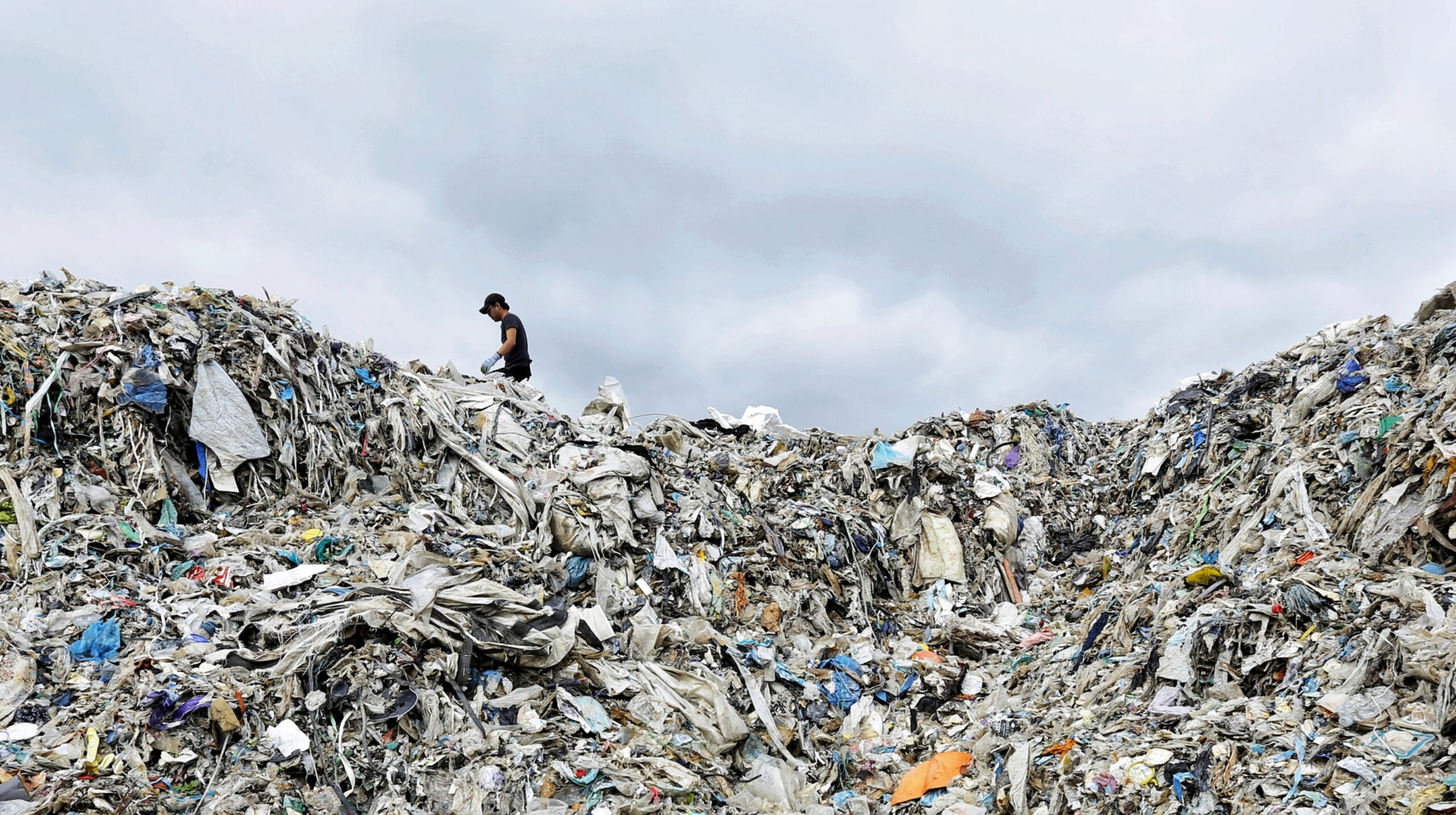 A worker stands at the top of a giant mound of plastic waste